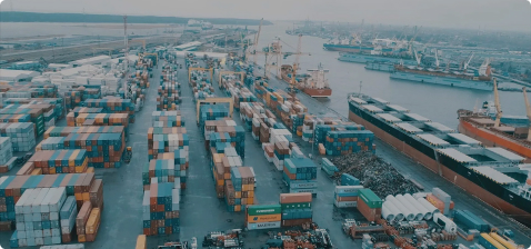 Панорамный вид на крупный морской порт с множеством контейнеровозов, включая судно Maersk Line, пришвартованных у причалов, и огромными складскими площадками, заполненными разноцветными контейнерами, снятый с высоты в ясный день