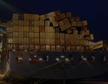 Грузовое судно с контейнерами, загруженное на фоне портовых кранов, освещенное огнями, ночью.