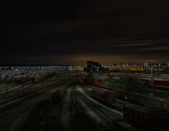 Ночной вид на большую железнодорожную станцию с многочисленными путями, вагонами различного типа и тепловозом с включенными фарами; освещенную фонарями, на заднем плане видны темные силуэты гор