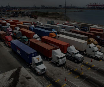 Фотография с высоким углом обзора, изображающая большое скопление разноцветных грузовиков с прицепами, стоящих в плотных рядах, создающих ощущение затора или ожидания