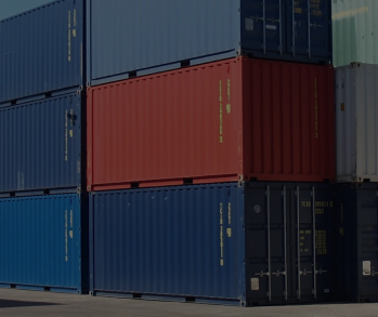 На фотографии изображены сложенные друг на друга морские контейнеры разных цветов: красные, белые и синие, при ярком солнечном свете и голубом небе