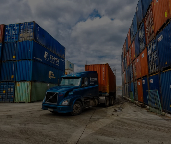 Фотография площадки с длинным рядом сложенных морских контейнеров разных цветов и логотипов, таких как 'TRANSIT' и 'PANDA EXPRESS LINE', на переднем плане грузовик без прицепа, пасмурная погода