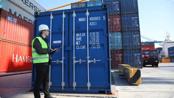 Сотрудник в каске и сигнальном жилете осматривает синий морской контейнер с табличкой 'MBBU 4000003', на заднем плане сложенные контейнеры, погрузчик и часть судна в порту
